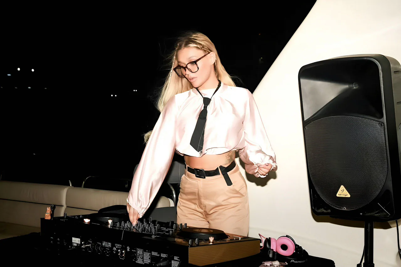 Zanna performing live on an open-air sunset terrace, wearing a white shirt and black tie