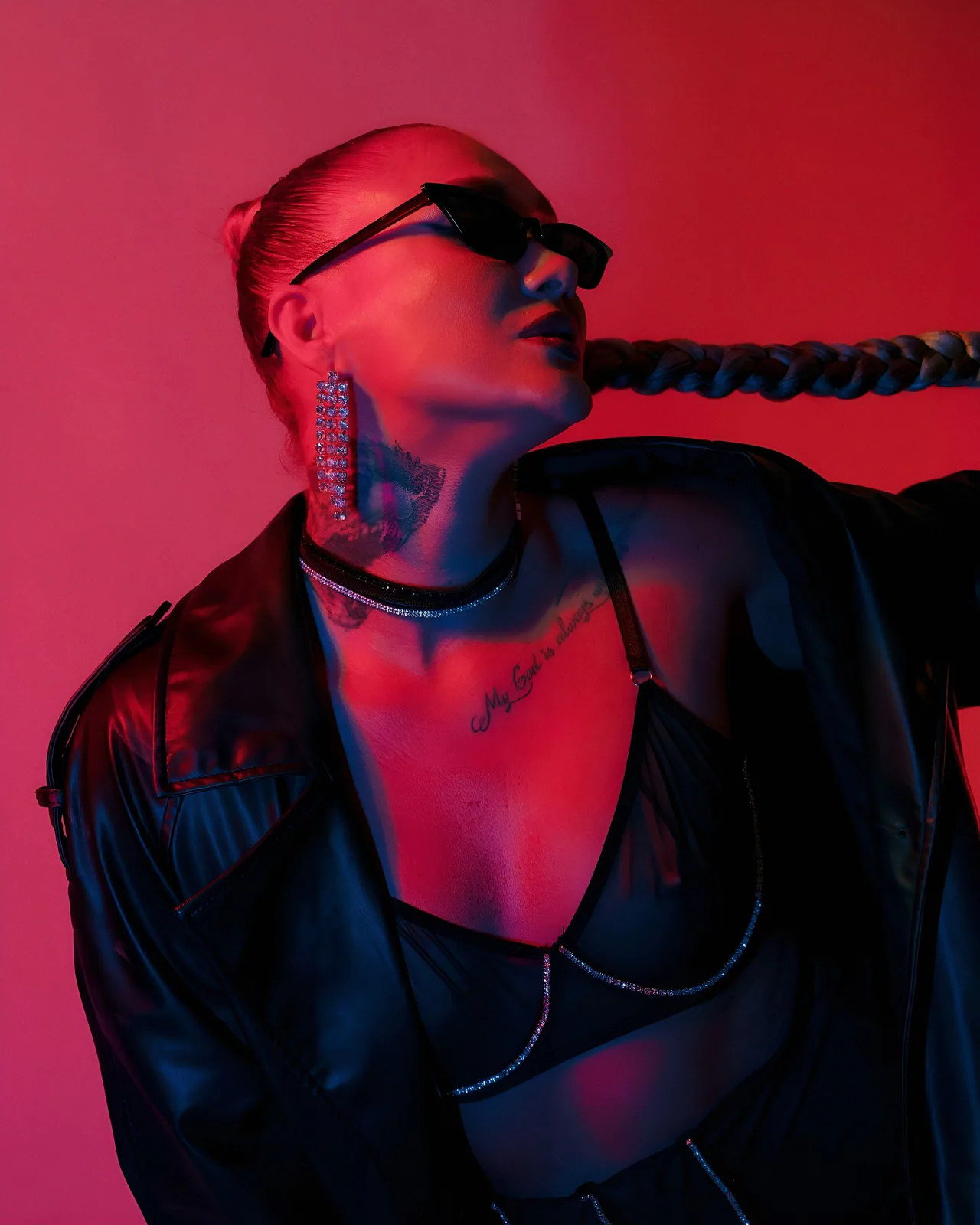 Zanna in sunglasses and a leather jacket under red and blue neon light